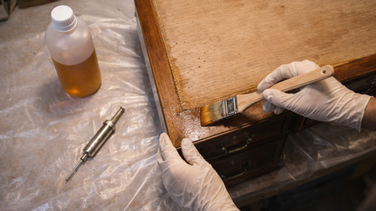 Traitement anti-vrillettes d'un bureau ancien dans un atelier de restauration avec pinceau et produit insecticide